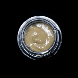 Cannabis concentrate in a glass jar on black background.