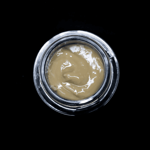 Cannabis concentrate in a glass jar on black background.